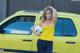 A woman holding a soccer ball in front of a yellow car.