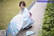 A woman in a blue kimono sitting on the ground with an umbrella.