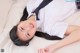 A woman in a school uniform laying on a white blanket.